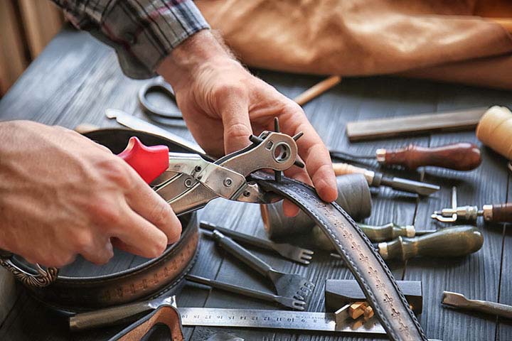 Which Tools Are Essential for Crafting Durable Belts & Bags?; Man using leather punch while working with belt at factory, closeup