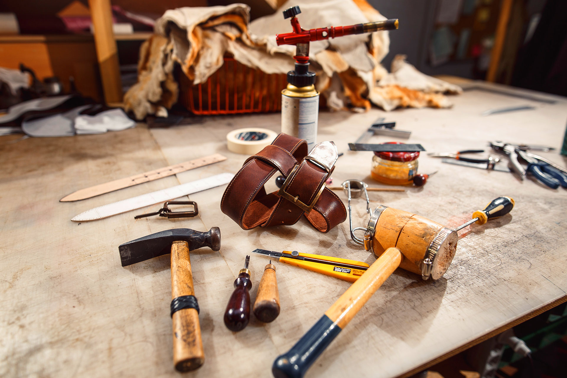 Leather crafting tools and a handmade brown belt spread across a workshop table
