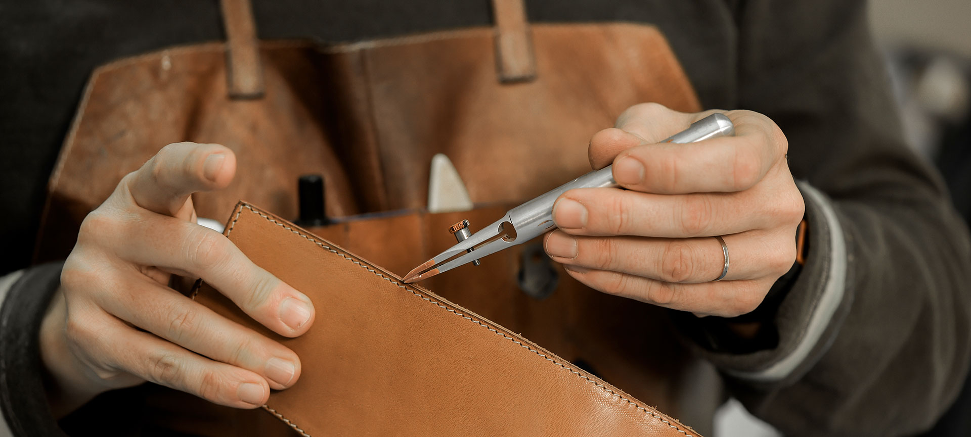 Artisan using a leatherworking tool to score stitching line on a tan leather bag