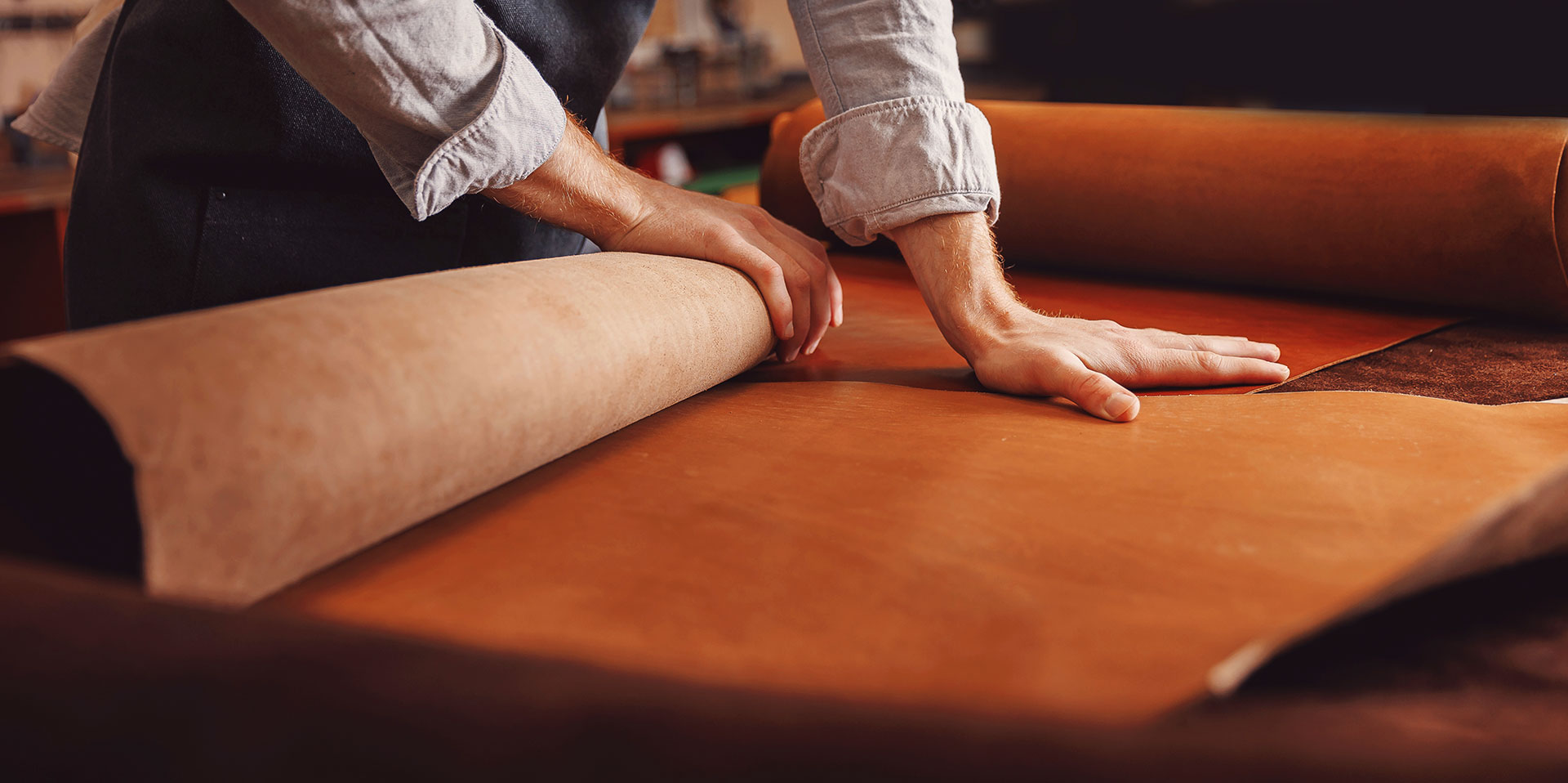 Hands rolling out large leather hides on workbench