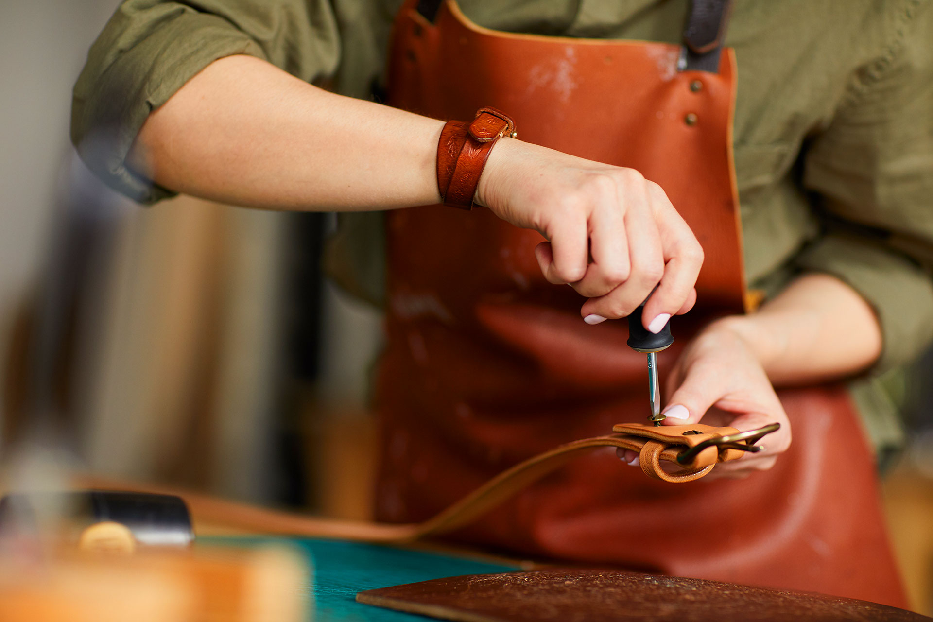 Craftsperson using screwdriver to assemble leather strap hardware