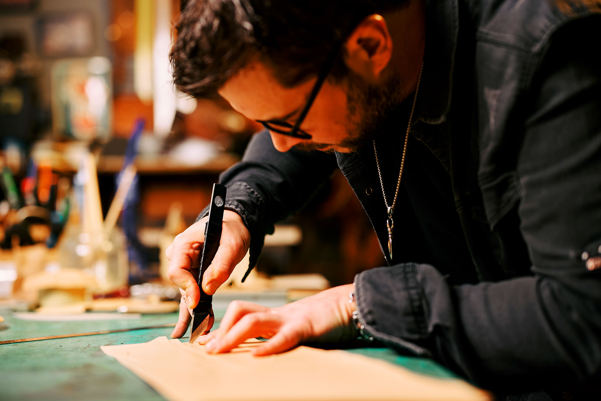 Leatherworker using utility knife to cut tan leather piece